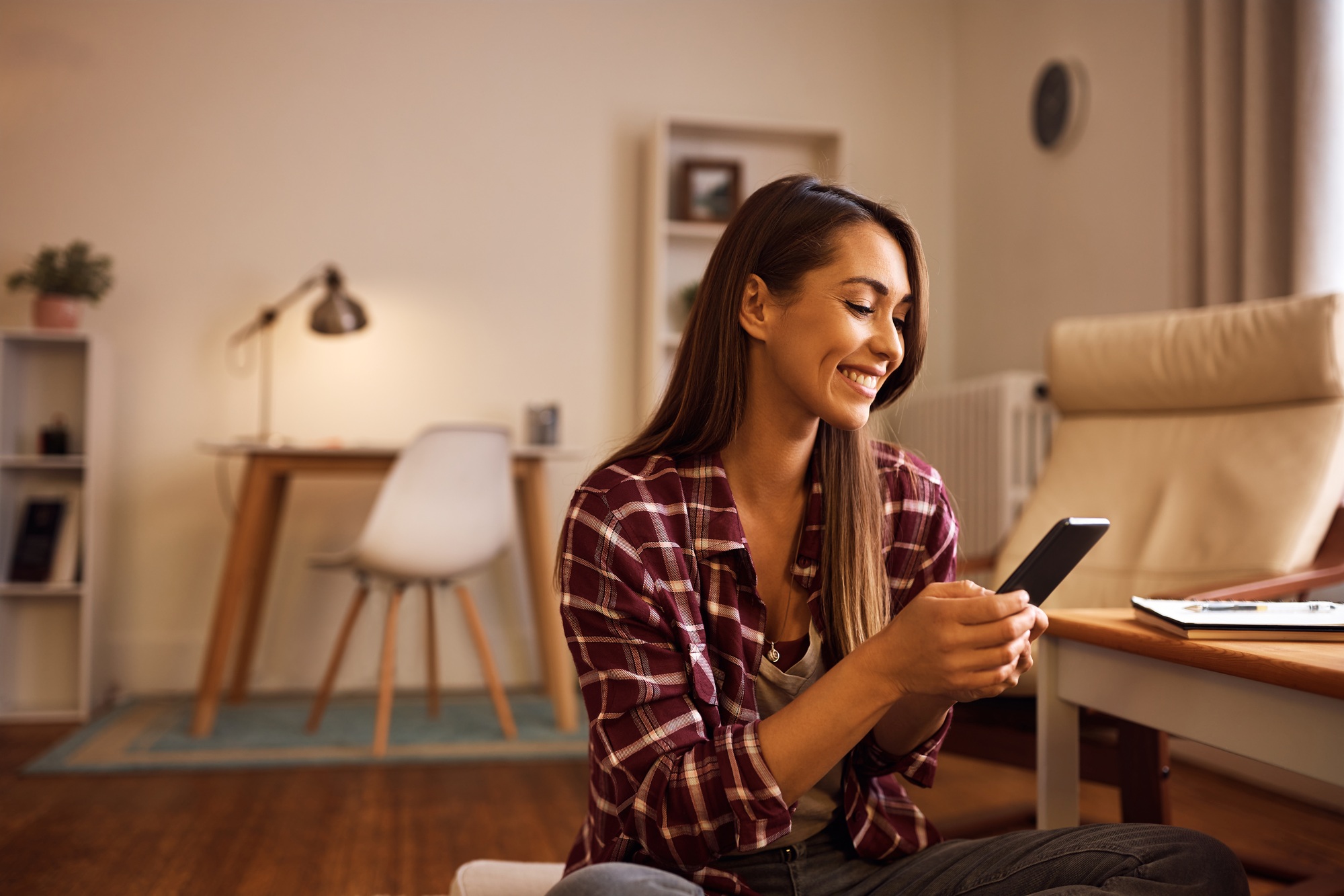 Happy woman text messaging on mobile phone at home.