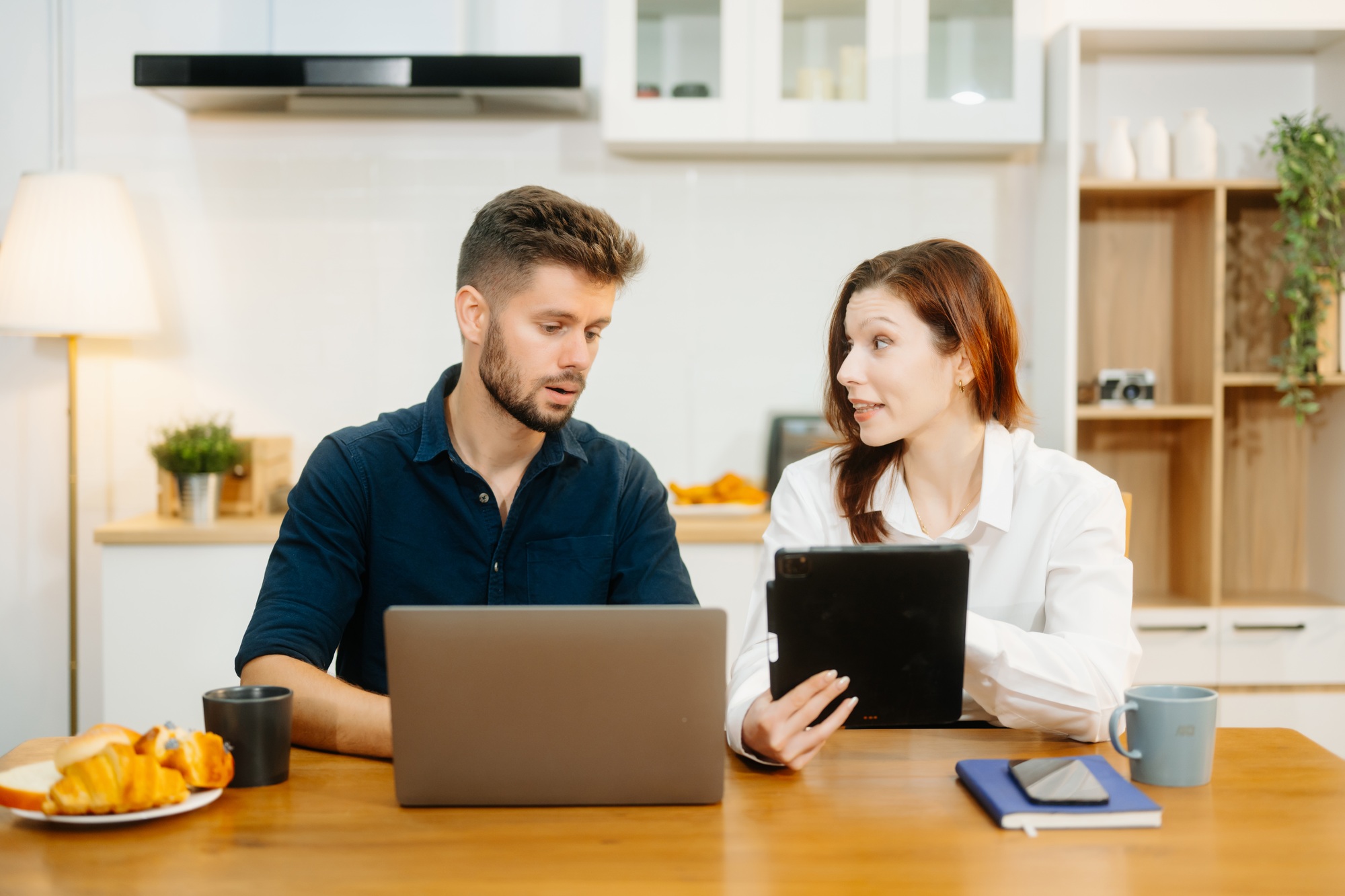 Modern couple collaborating over coffee in a cozy kitchen setting with a laptop, notebook, and