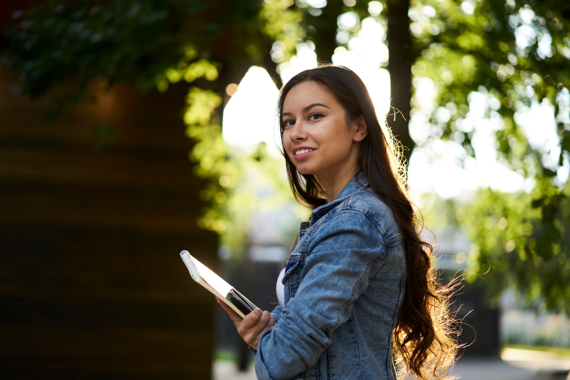 Happy Caucaisna female student with personal planner enjoying sunny weather for learning on nature