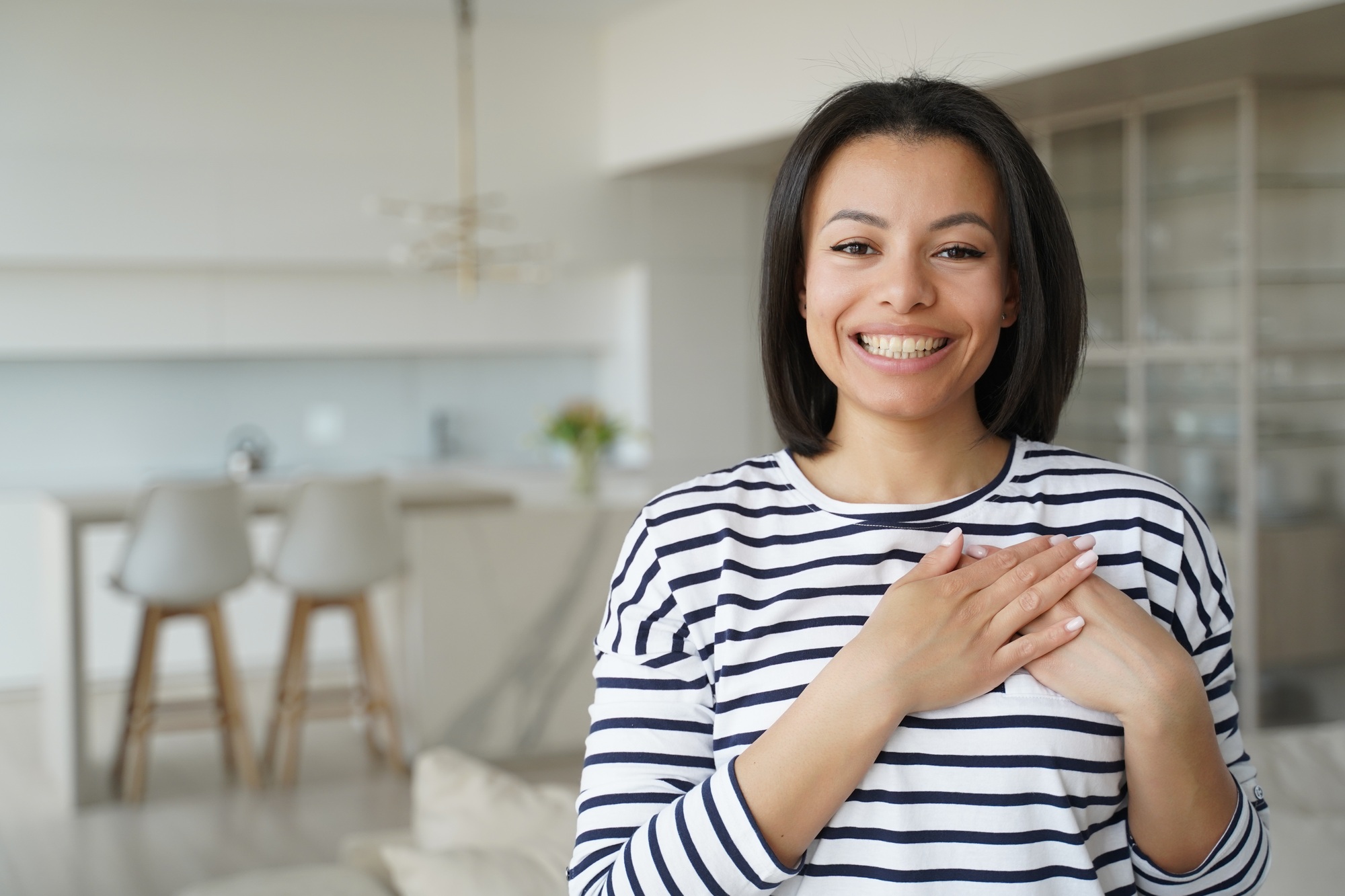 Touched thankful woman thanks smiling, holding hands on chest feeling love, appreciation at home
