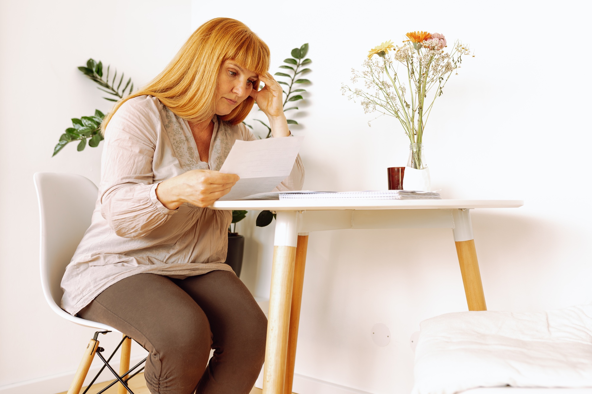 blonde woman reading letter notice while sitting at table in room